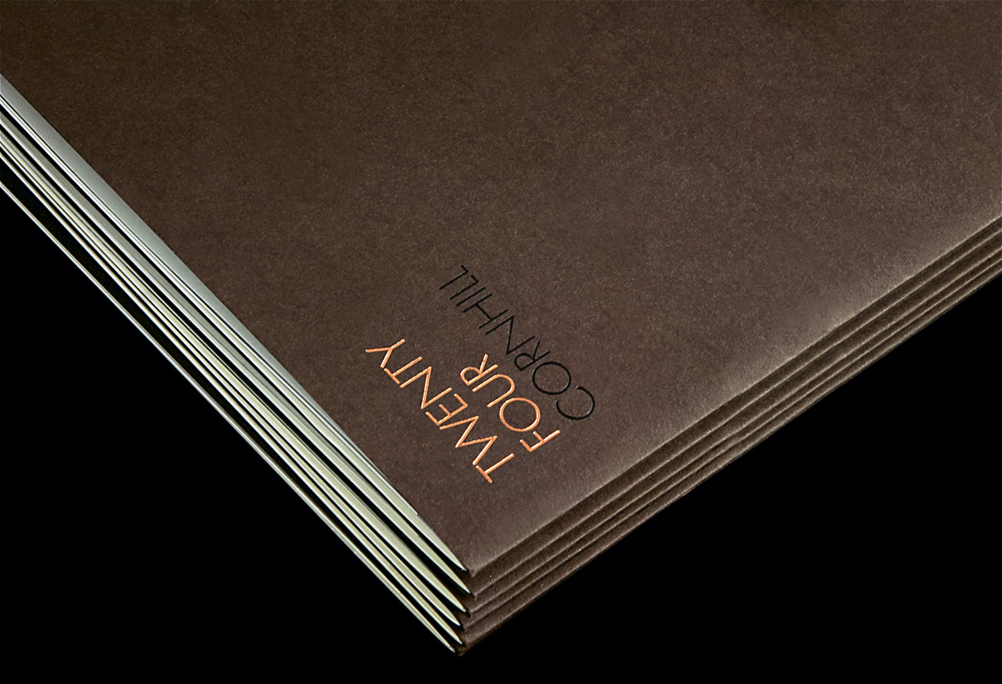 The corner of a dark brochure, Twenty Four Cornhill blocked in copper on its cover.