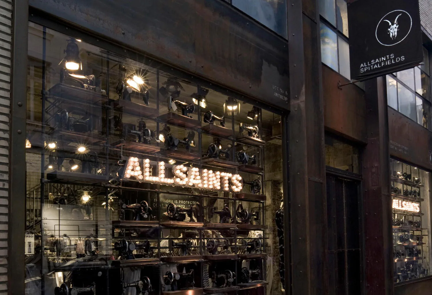 The AllSaints shopfront at night, its window filled with rows of lit vintage sewing machines.