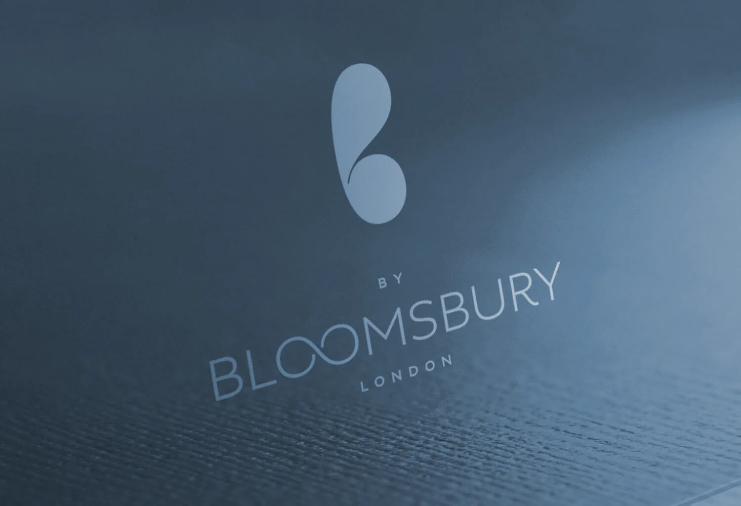 The monogram and wordmark blind-embossed into teal board.