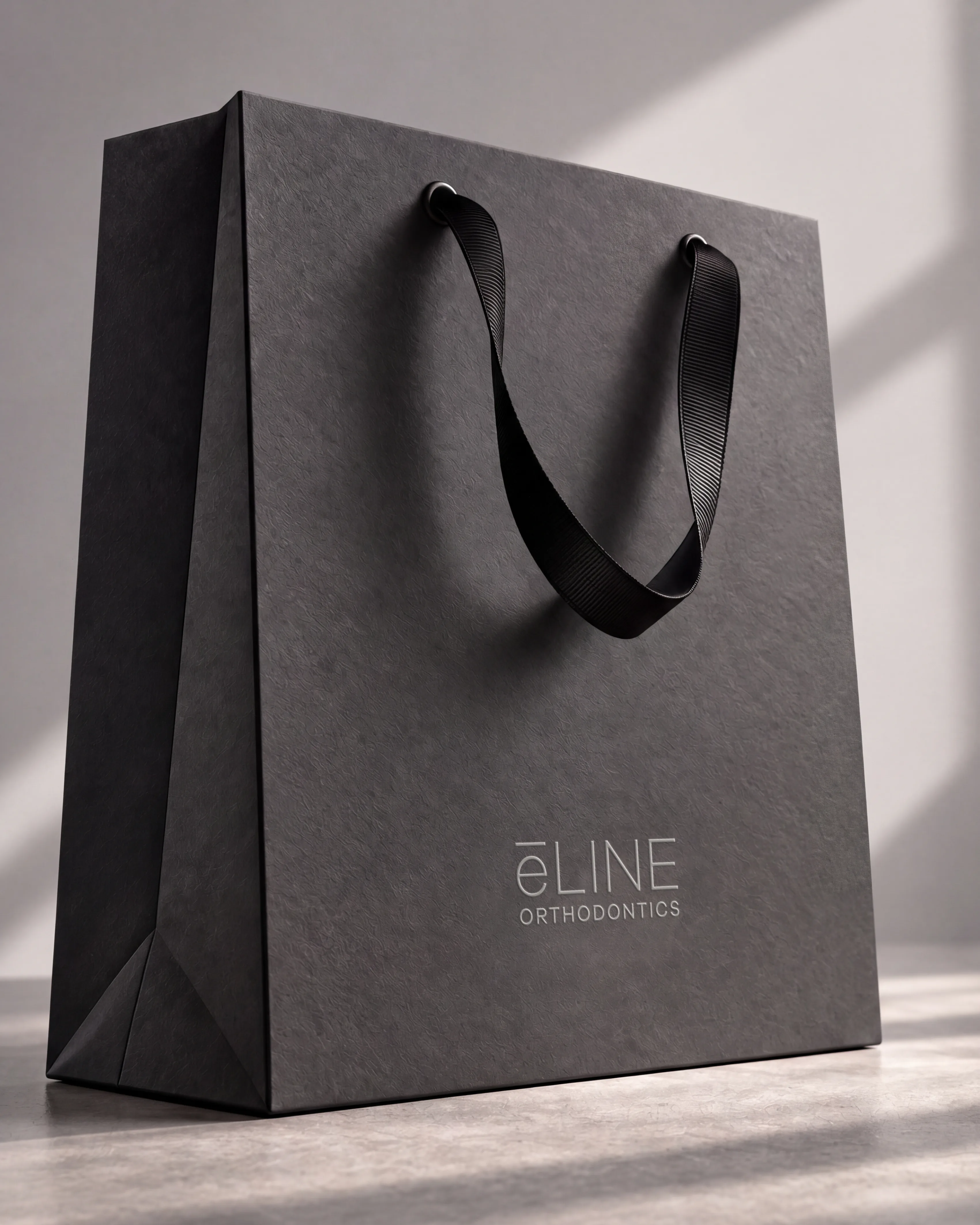 e-LINE Orthodontics carrier bag in charcoal board with a silver foil logo