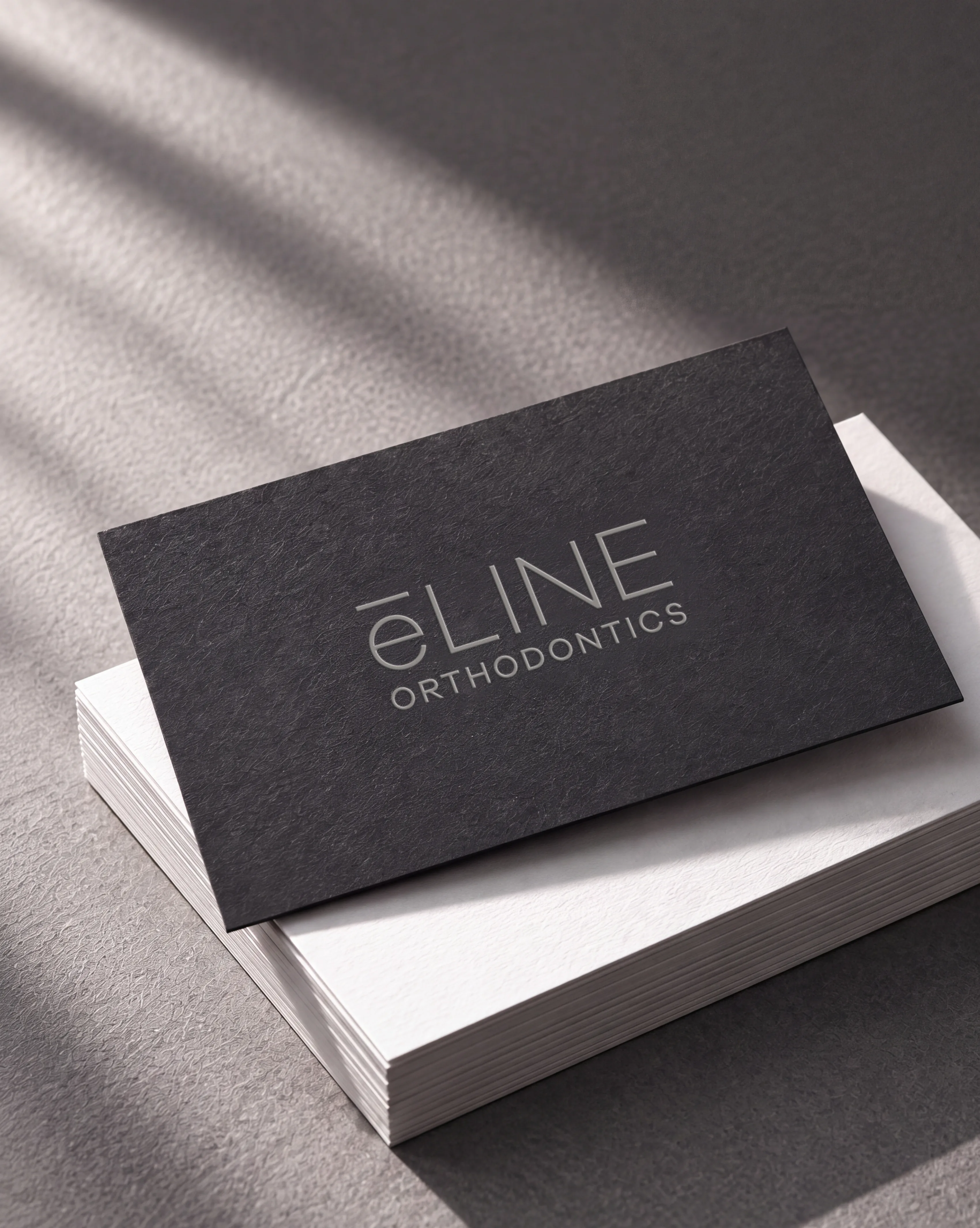 e-LINE business card in charcoal with a silver foil logo, on a stack of white cards