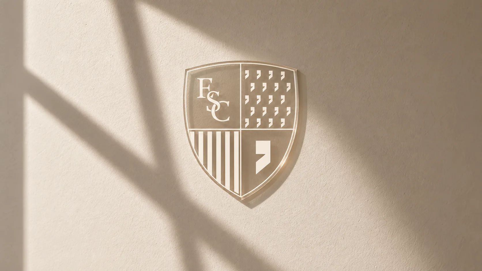 The Elsewhere crest raised in clear relief on a cream plaster wall, cut by a hard diagonal shadow.