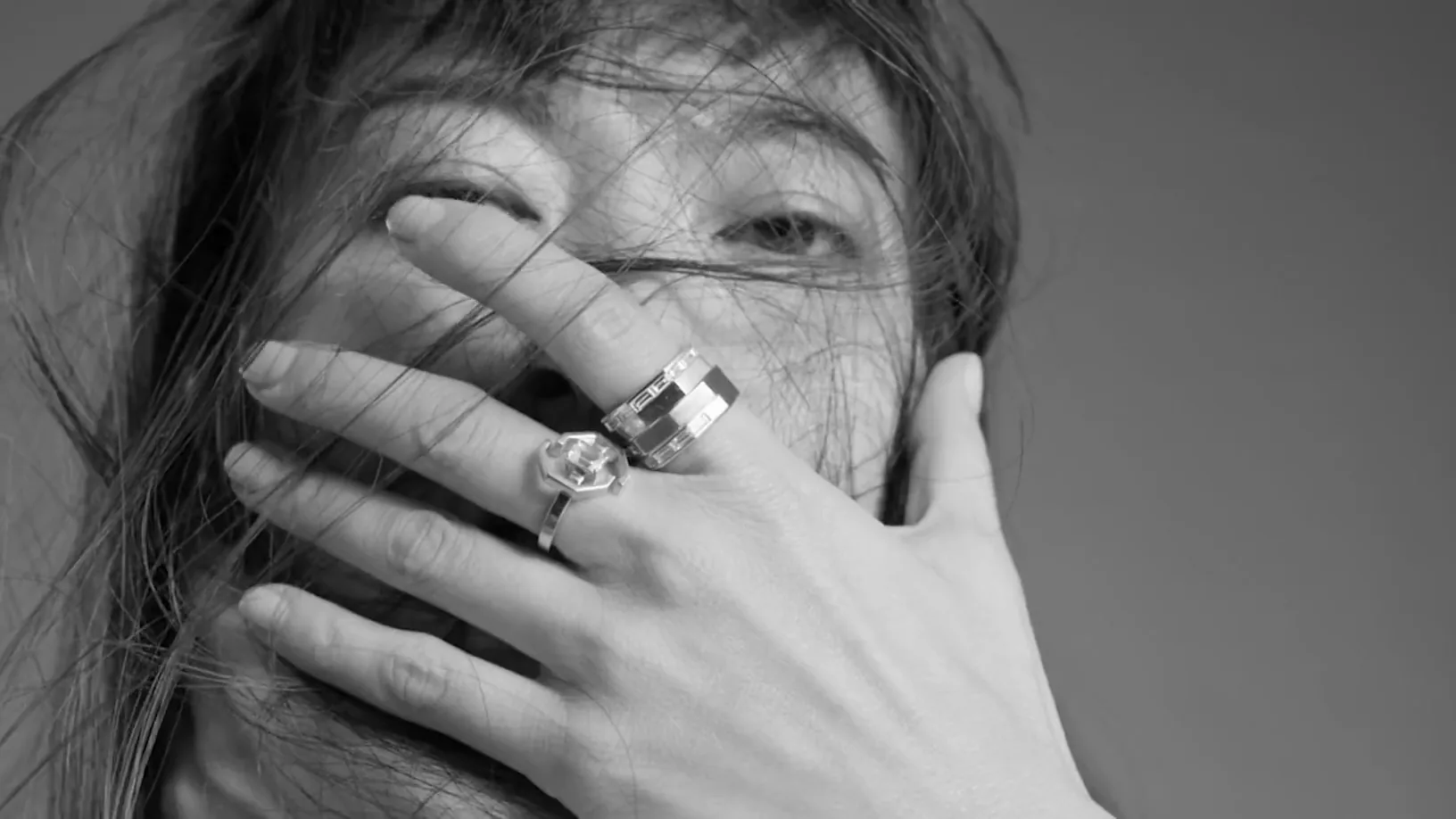 Rings and bangles in close black and white, a hand held across the model's face.
