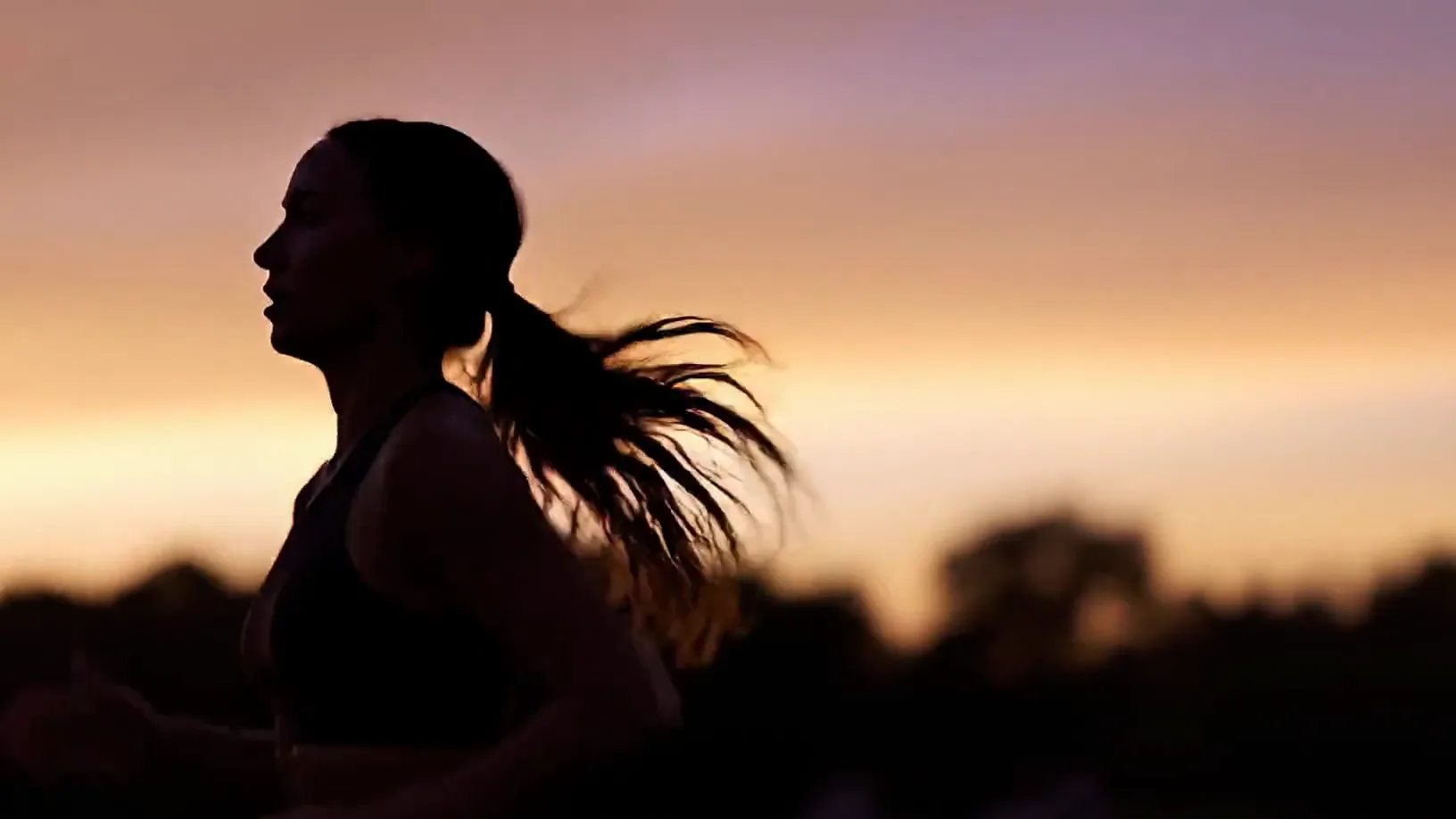 A runner in silhouette keeping pace against an amber sunset, a dark treeline beyond.