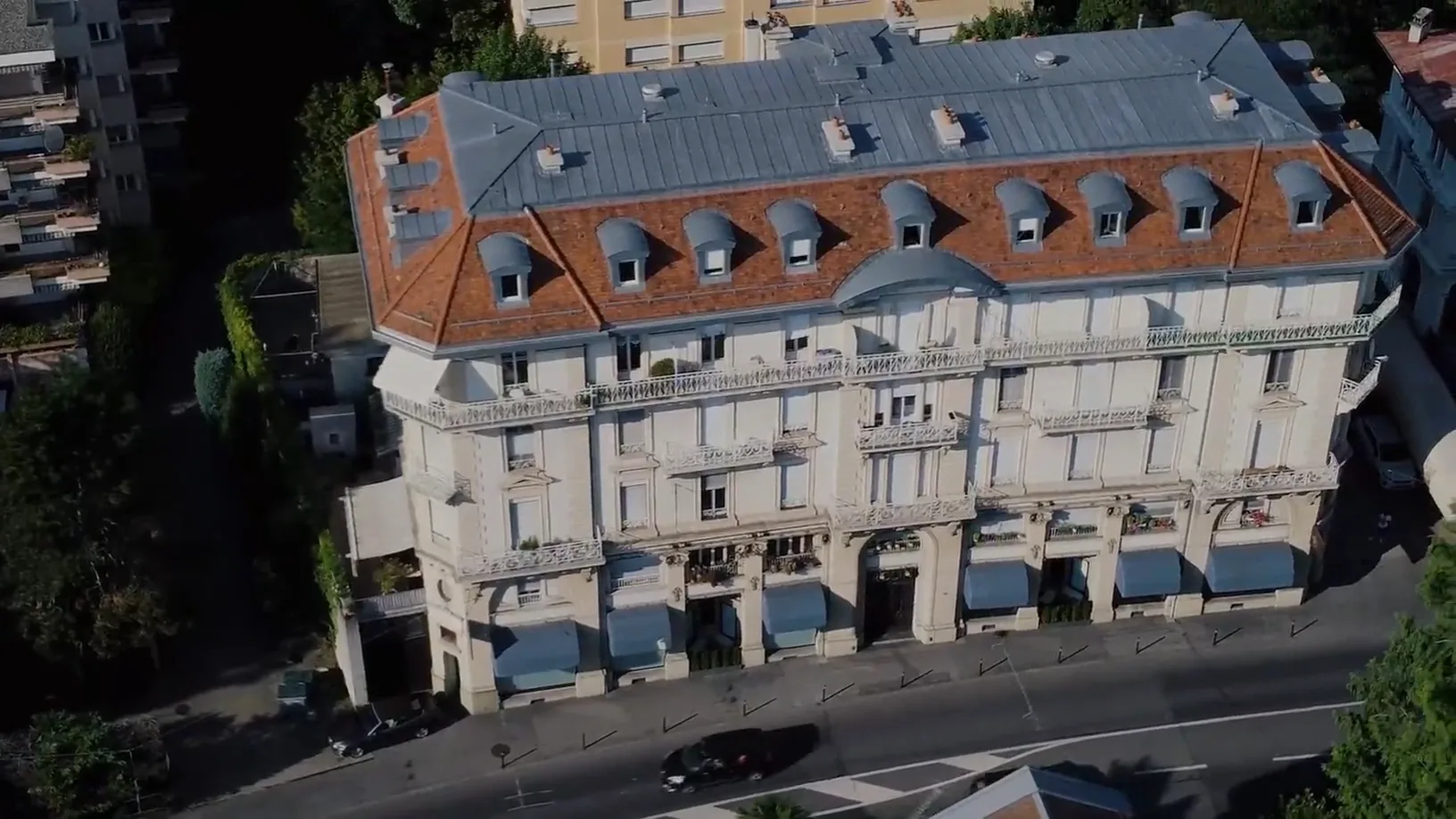 An aerial over a red-roofed building at Montreux, then the lake and wooded ridges above it.