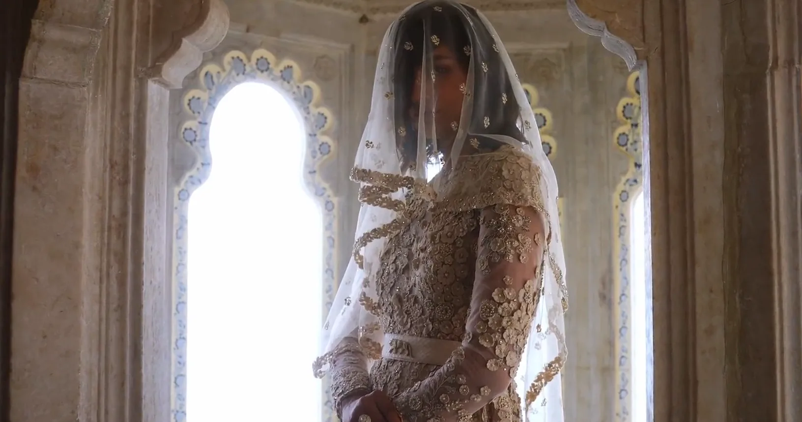 A veiled bride at an arched window, then in profile in a garden of white flowers.