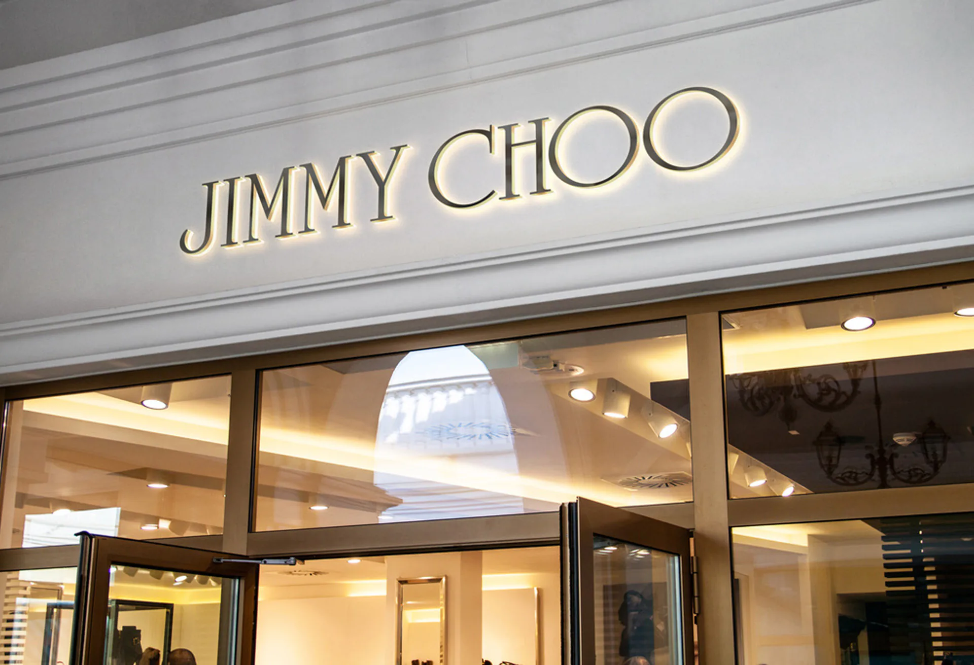 The Jimmy Choo shopfront at night, gold lettering above lit display windows.