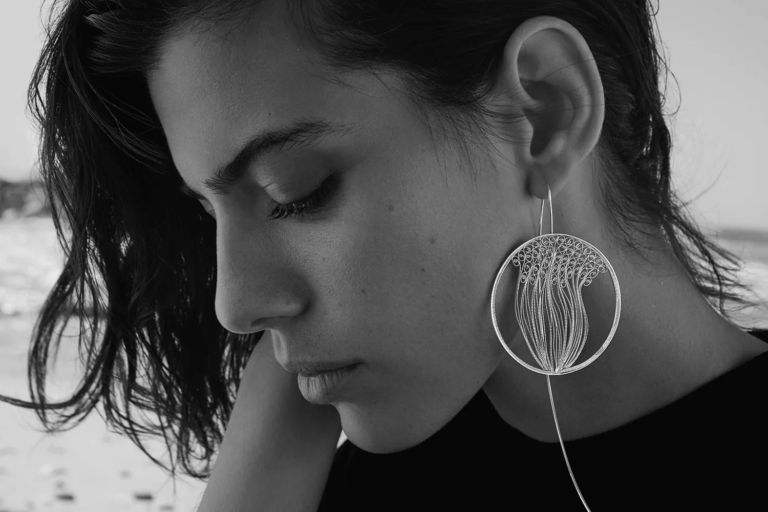 A close black and white portrait, the model looking down, wearing a large filigree drop earring.
