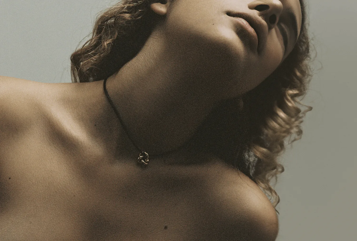 A fine chain and small pendant at the base of a model's throat.